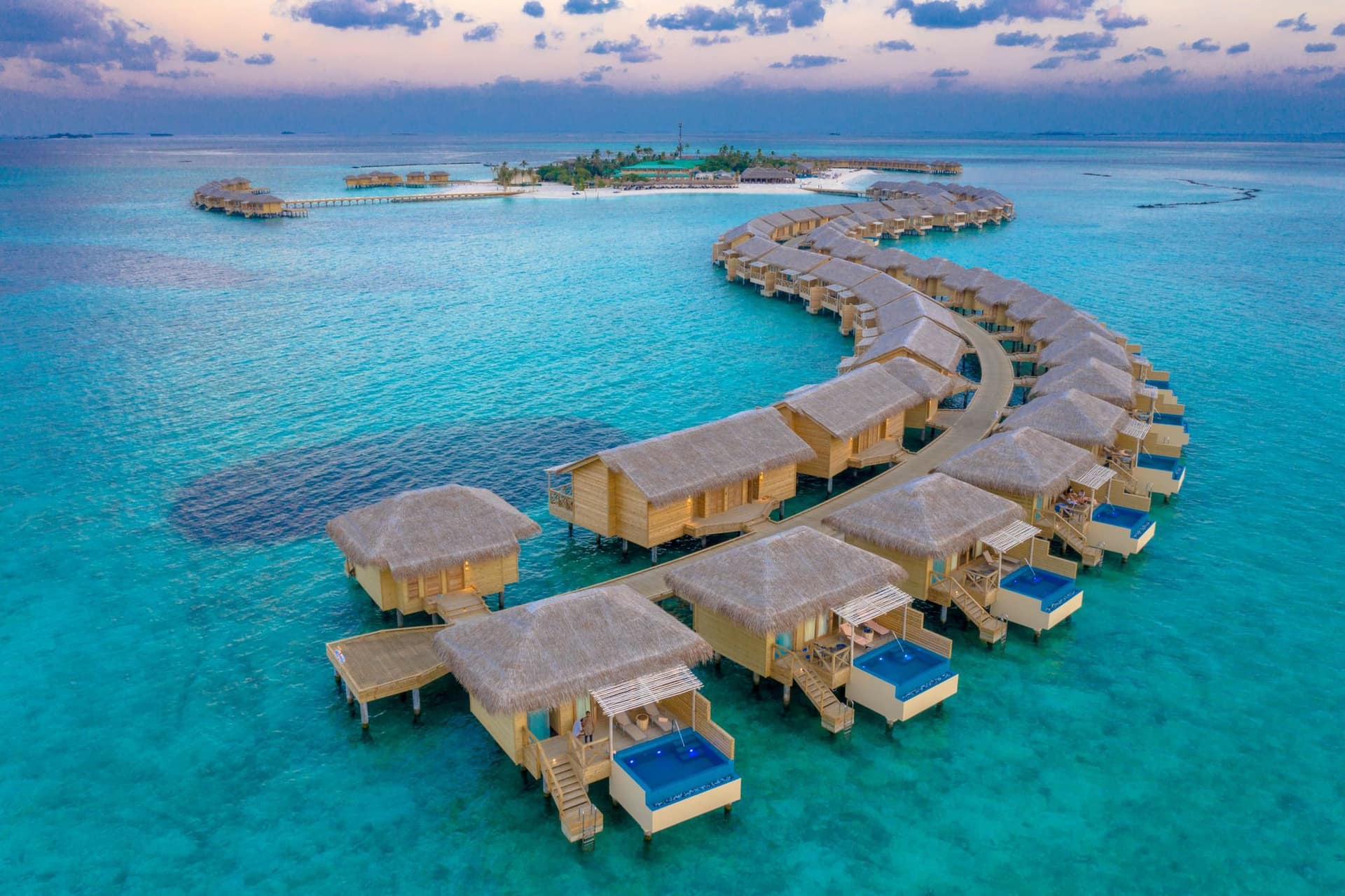 Overwater villas glowing at sunset above a calm Maldives lagoon